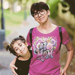 Adult wearing a bright pink “#1 Mom” floral T‑shirt while standing with a child outdoors